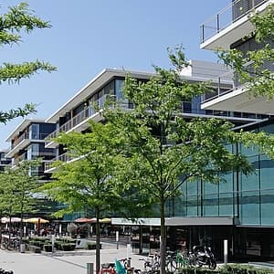 Moderno complesso edilizio con facciata in vetro, alberi e biciclette su una strada trafficata