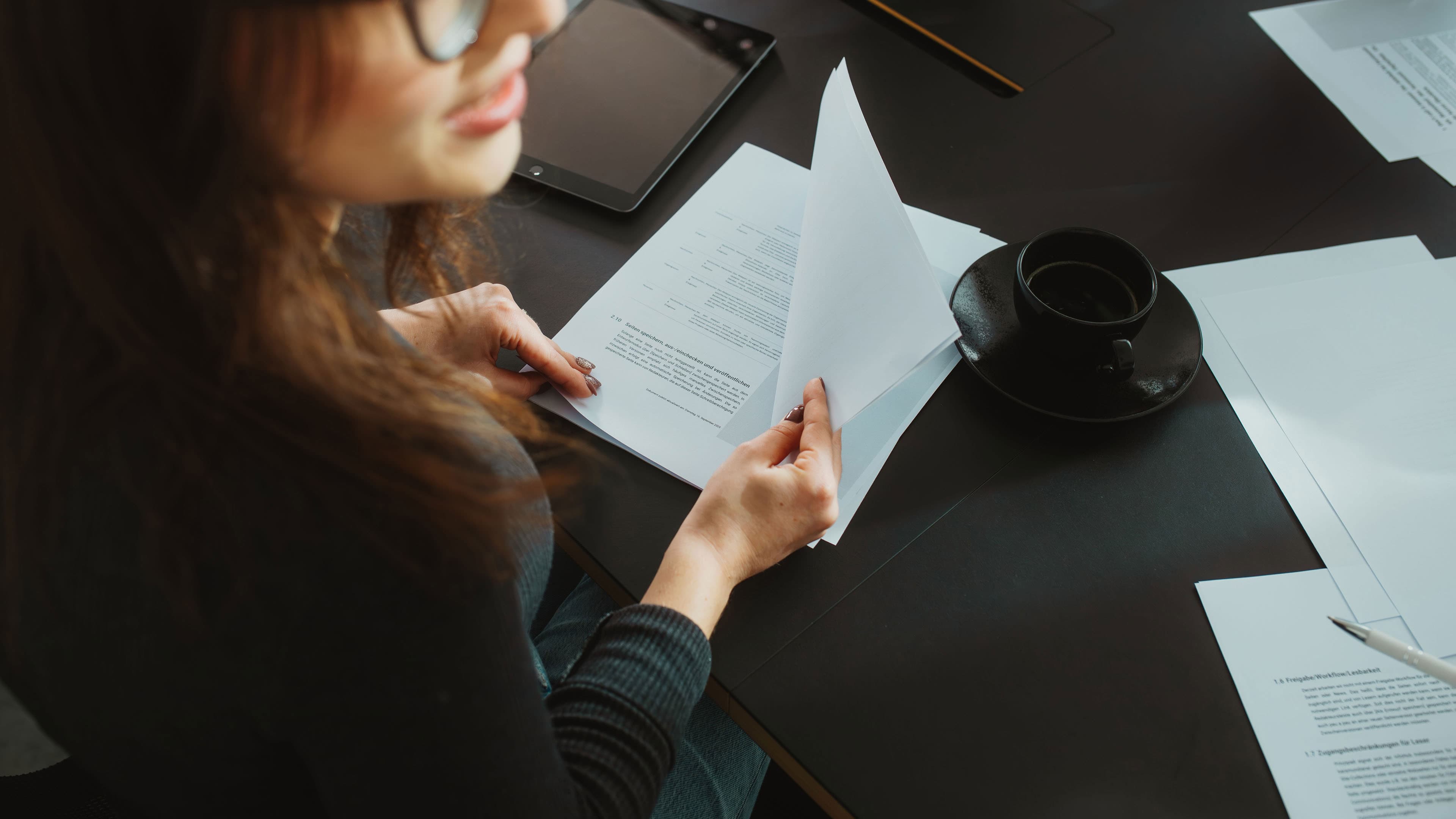 A person is reviewing documents at a table next to a tablet and a coffee cup