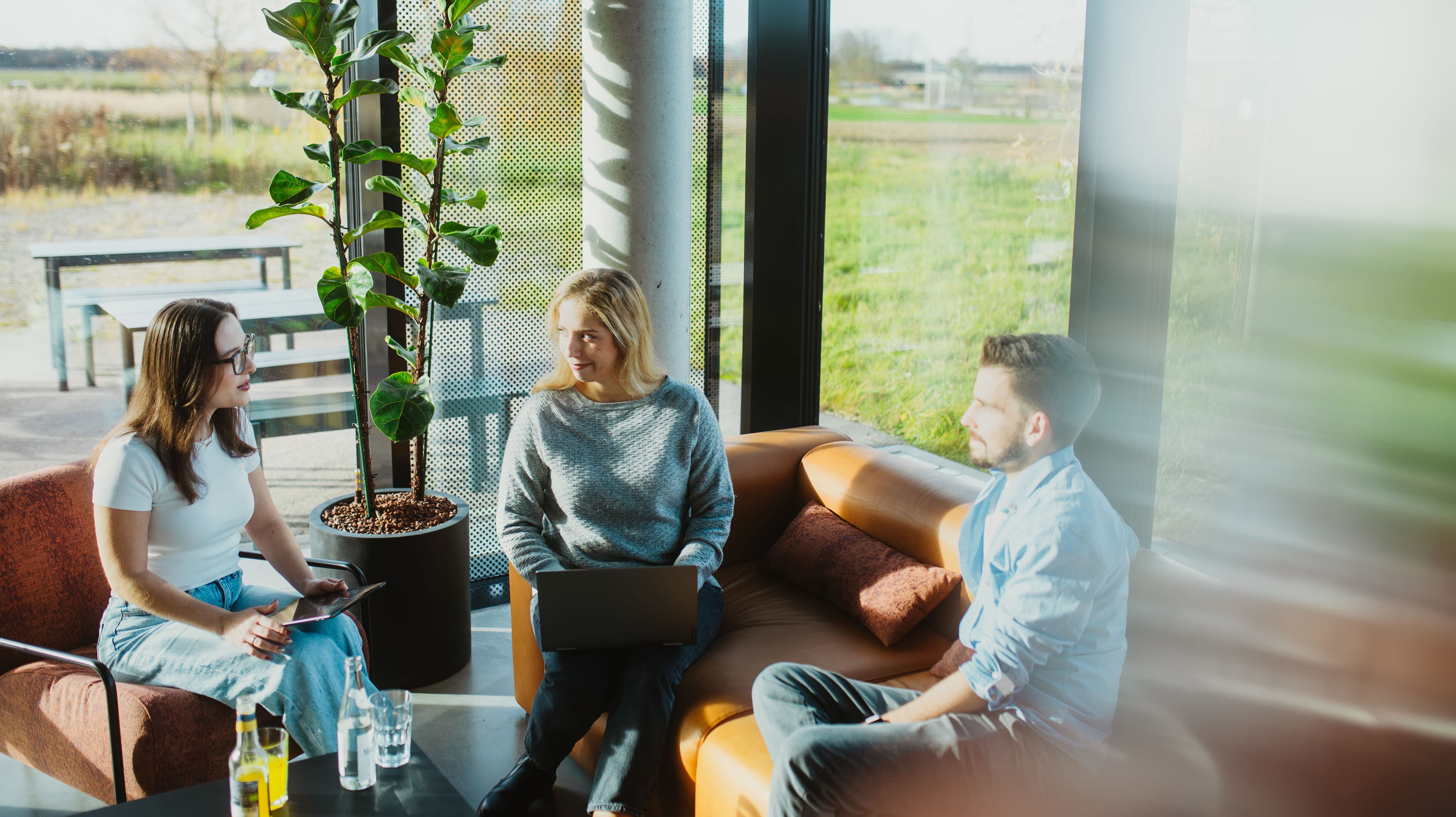 Drei Personen arbeiten in einem hellen Café an Laptop und Tablet.