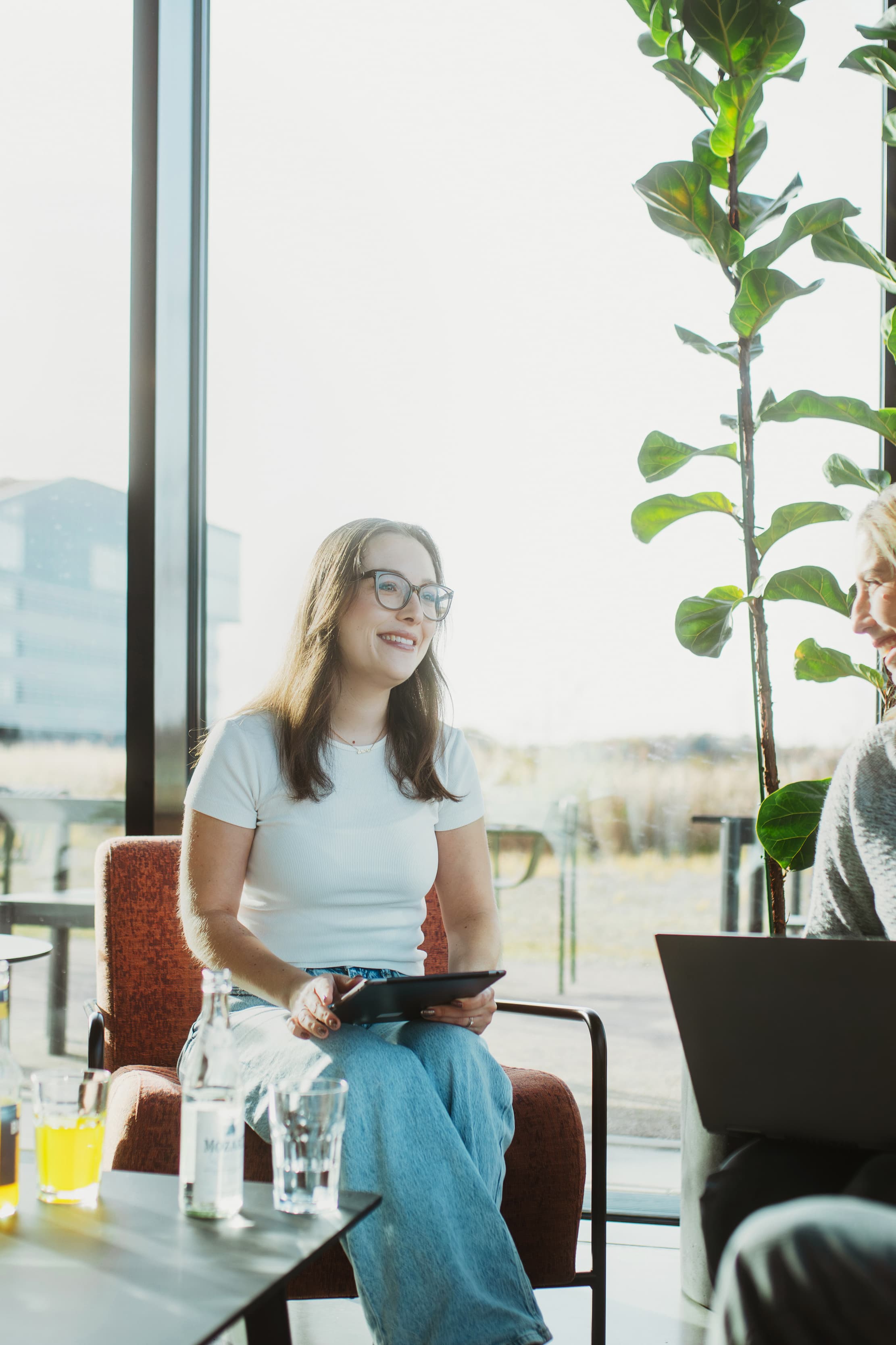 Two women are sitting in a well-lit office, working on a tablet and a laptop.