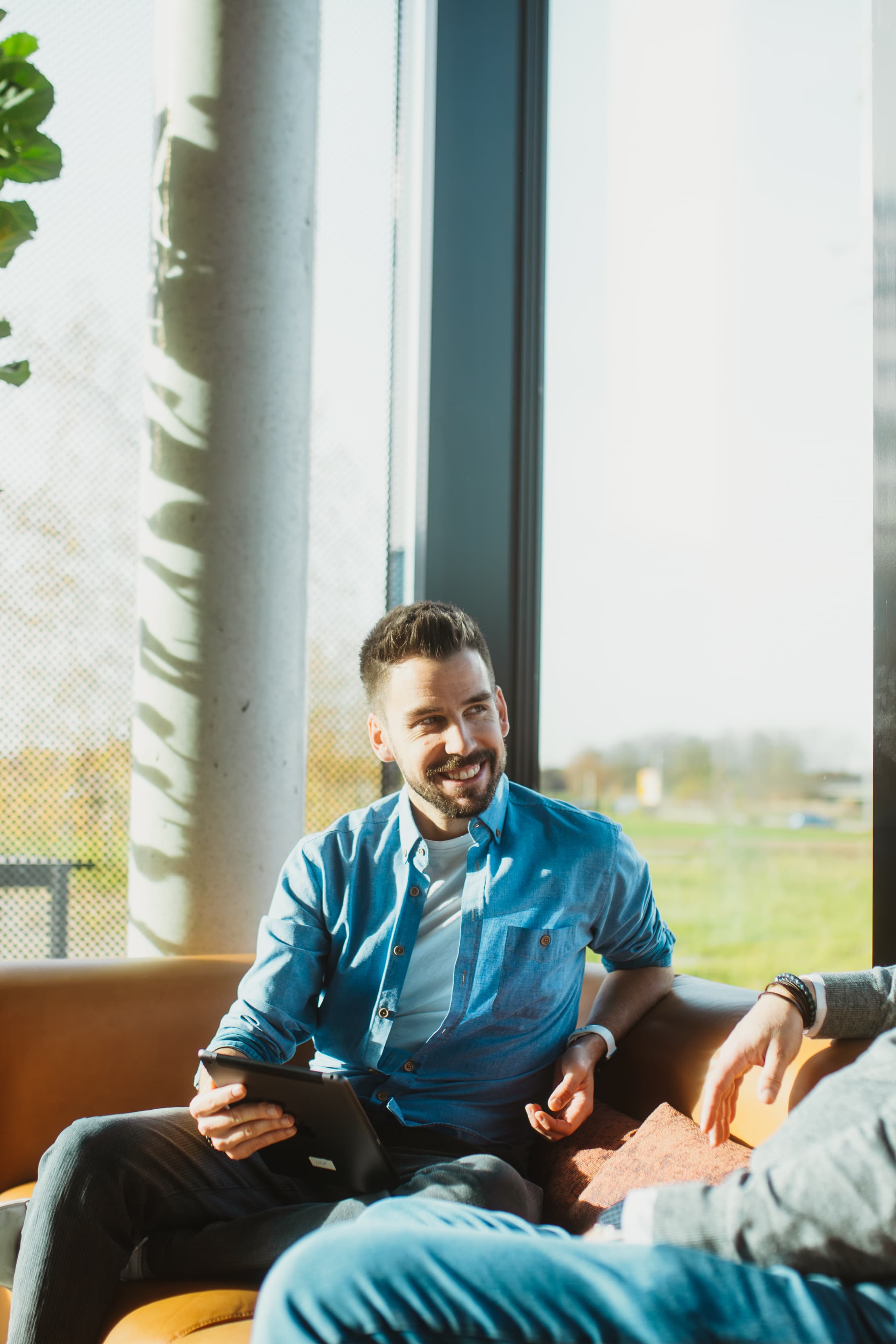 Zwei Kollegen im Gespräch mit Tablet in einer sonnigen Lounge