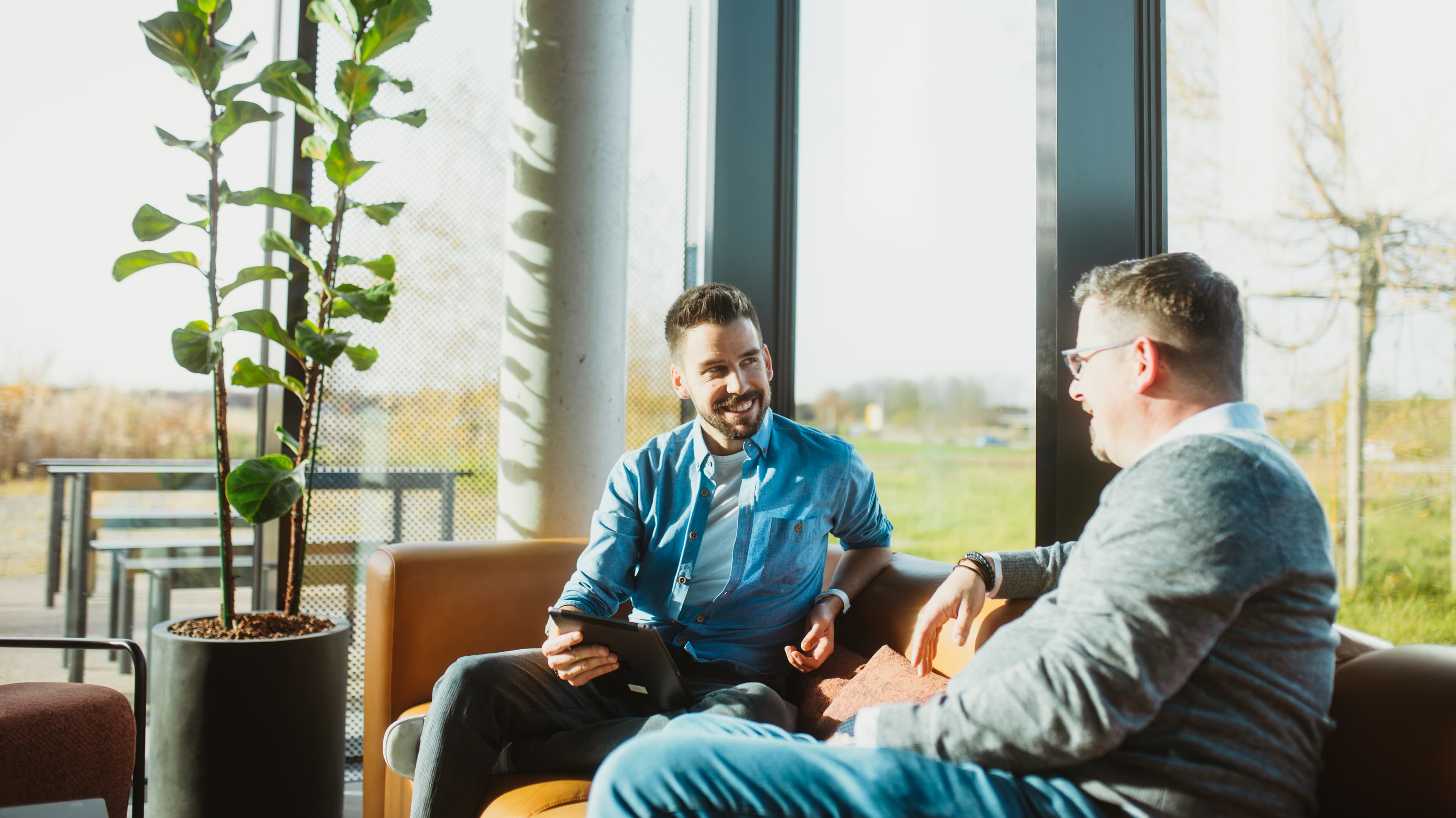 Zwei Kollegen im Gespräch mit Tablet in einer sonnigen Lounge
