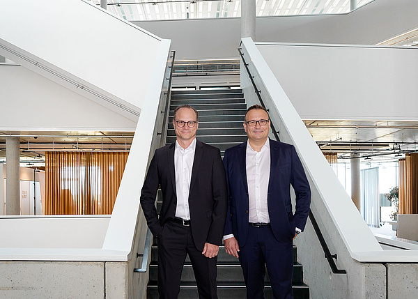 Die Geschäftsführer Michael Huber und Lars Rippert von baramundi stehen vor einer Treppe in einem modernen Bürogebäude