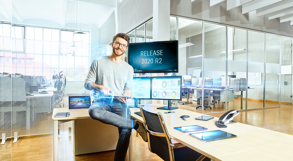 Mann im Technologiebüro vor Bildschirmen mit Release-Ankündigung "Release 2020 R2"