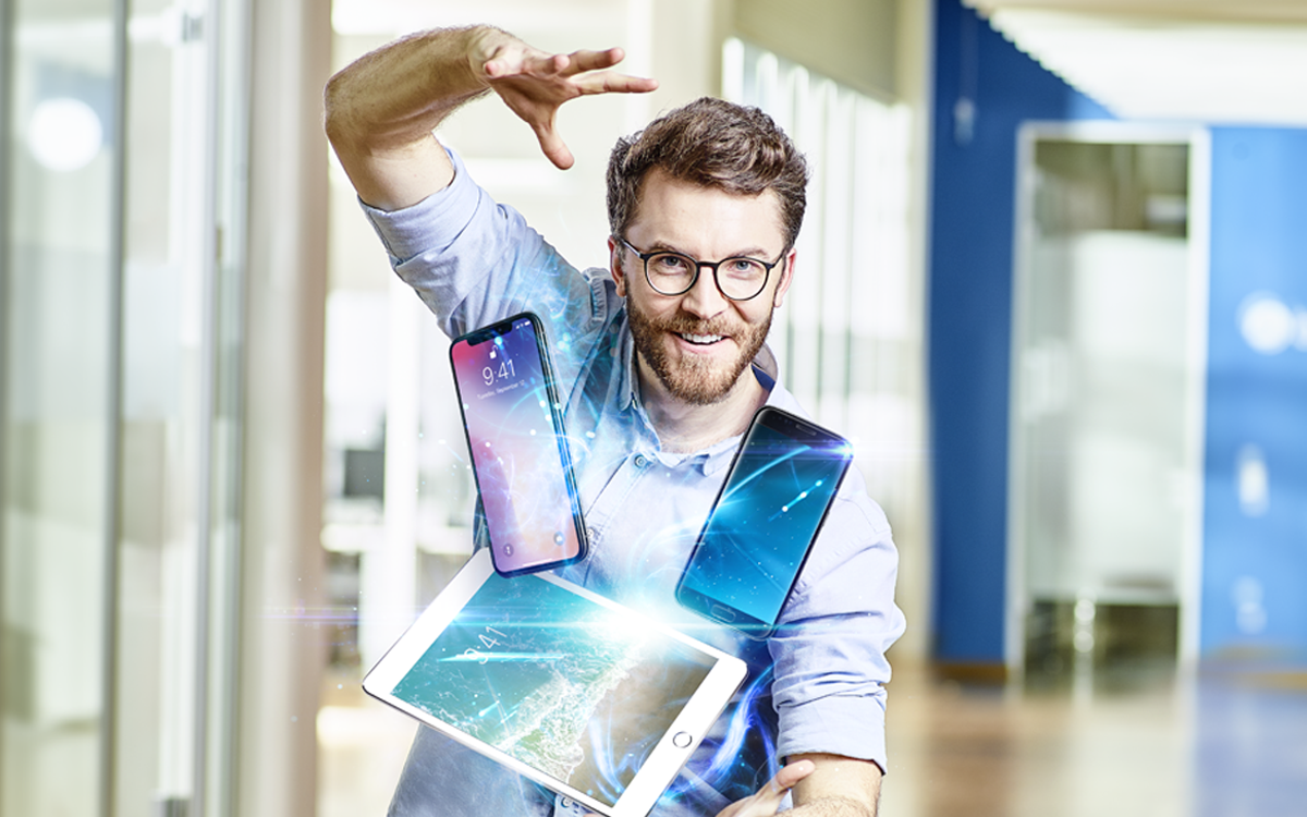 Ein fröhlicher Mann, der mehrere mobile Geräte mühelos in der Luft jongliert, um Enterprise Mobility Management zu demonstrieren