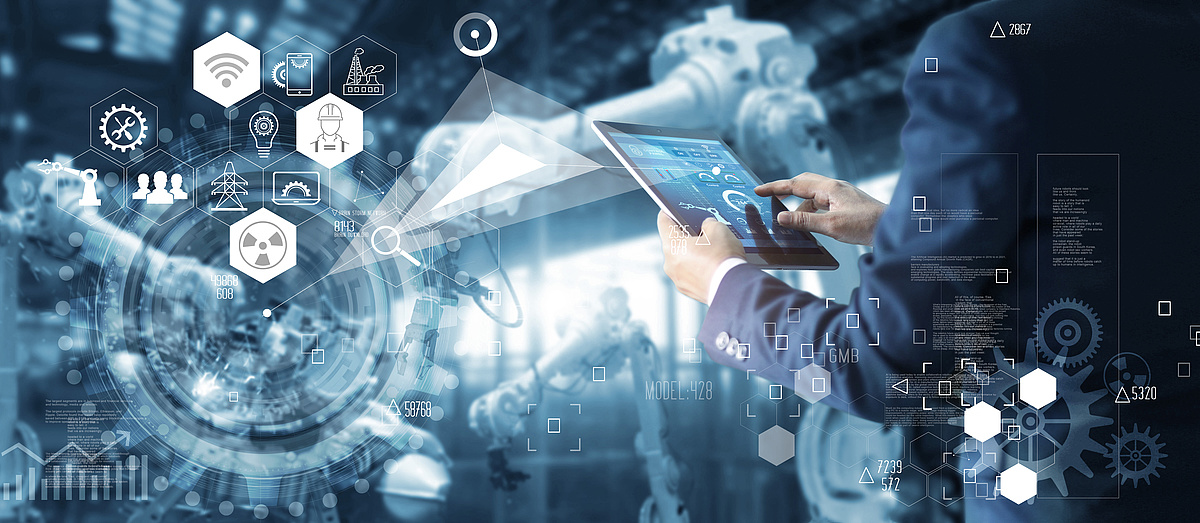 Ein Mann in einem Anzug verwendet ein Tablet, um eine industrielle Automatisierungssoftware in einer modernen Fertigungsanlage zu steuern